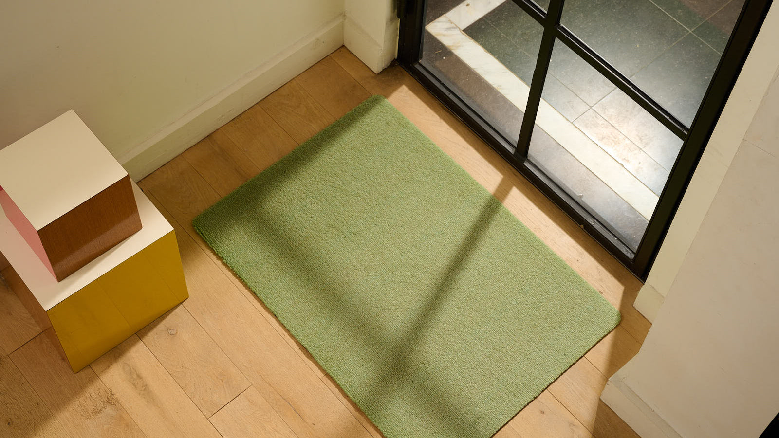 Modern entryway with a green doormat on wooden flooring near a glass door, providing dirt trapping and a stylish, fresh accent to the space.