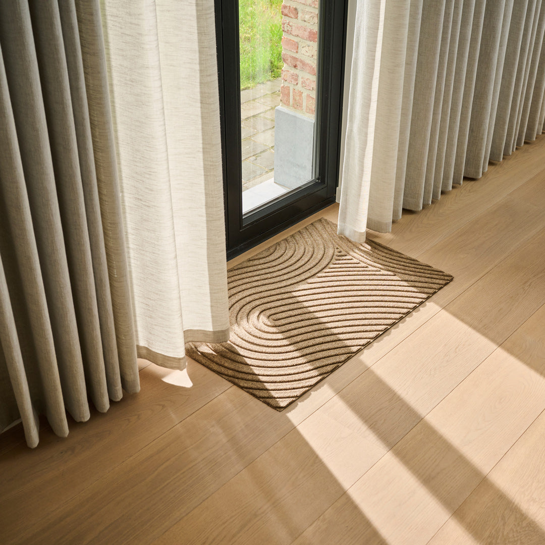 Lifestyle photo showing WaterHog All-Weather Indoor Outdoor Floor Mat in use at a door with curtains inside a nice and cosy interior design home in beige and warm tones