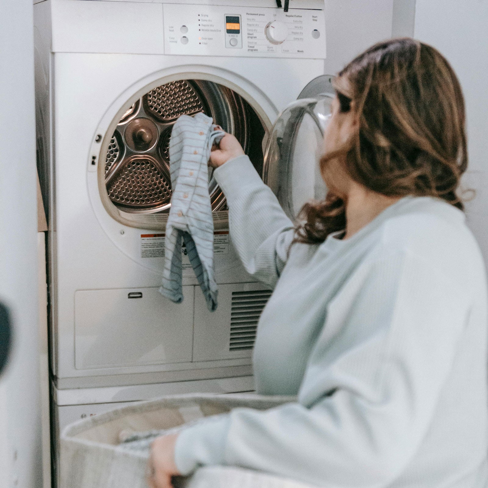 A woman in a green shirt loads beige laundry into a front-loading washing machine in a bright,